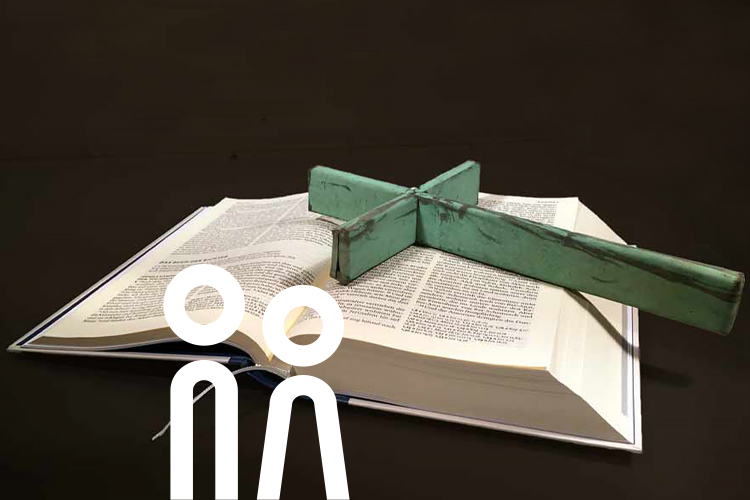Aufgeschlagene Bibel mit einem kleinen Kreuz der Gemeinde darauf liegend.