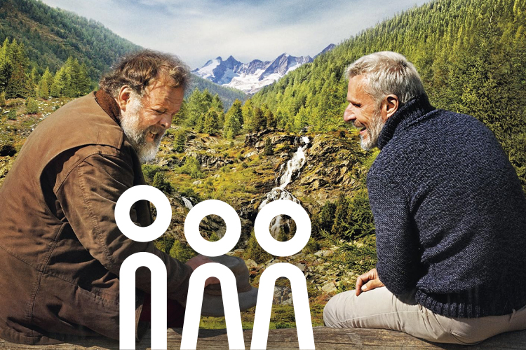 Szene aus dem Film: beide Hauptdarsteller lachend auf einer Bergwiese.