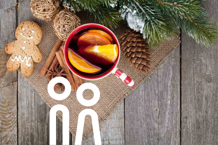 Tasse mit Glögi und Scheiben einer Orange, eine Pfefferkuchenfigur, Zimstangen und ein Tannenzweig, von oben auf auf einer Holzplanke.
