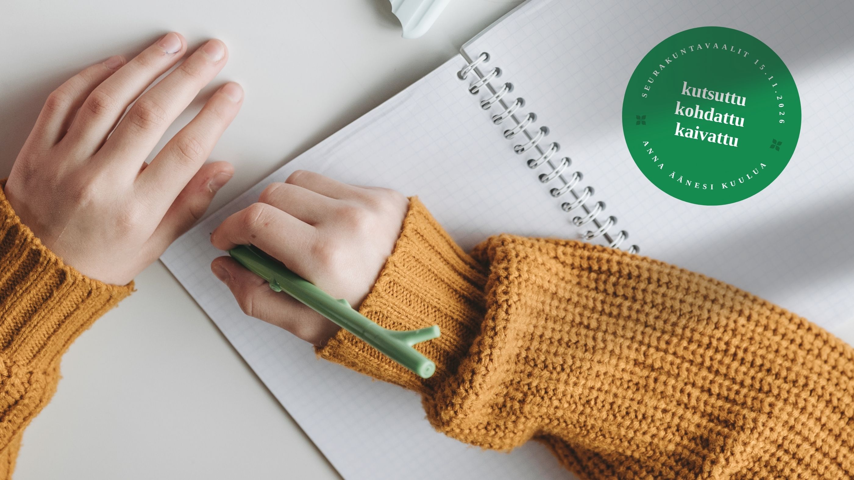 Zwei Unterarme im Wollpullover, mit einem Stift in der Hand, auf einem Notizheft.